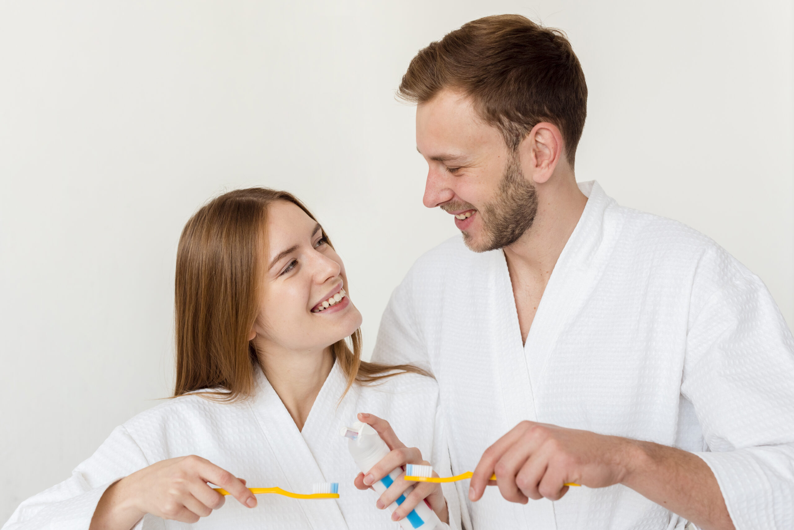 couple-bathrobes-holding-toothbrushes-looking-each-other